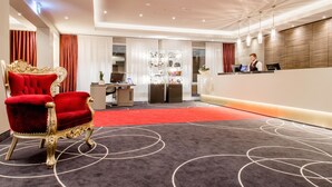 A hotel reception area with a red carpet, a reception desk, and a red velvet chair. - Hotel Fulda Mitte (Fulda)