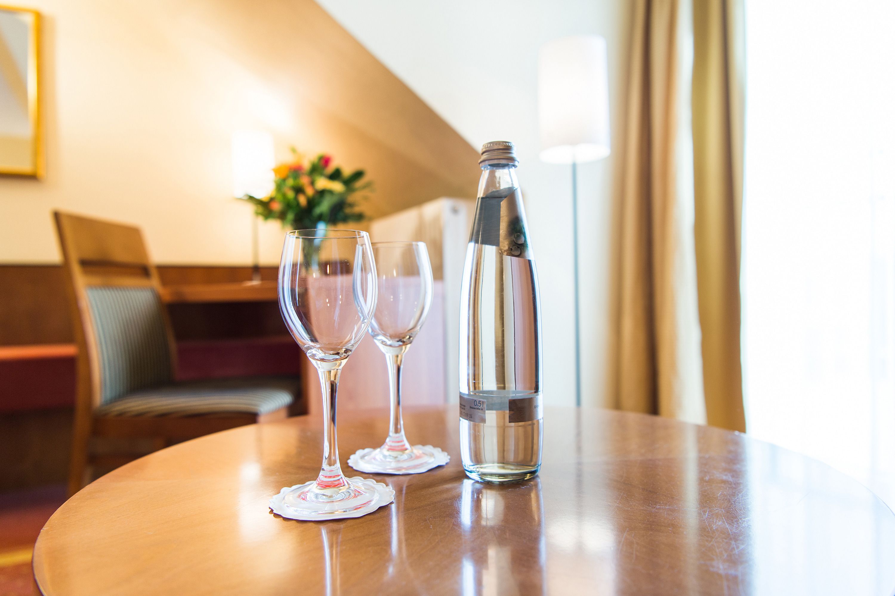 A round wooden table with two empty wine glasses and a water bottle.