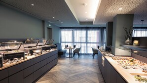 A modern breakfast buffet with a variety of food options, a seating area with chairs, and large windows providing natural light. - Hotel Fulda Mitte (Fulda)