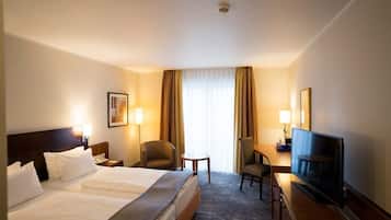 A hotel room with a large bed, a desk with a television, a chair, and a small table.