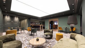 A hotel lobby with a high ceiling, marble flooring, and modern furniture including sofas and chairs. There is a bar area in the background. - Hotel Fulda Mitte (Fulda)