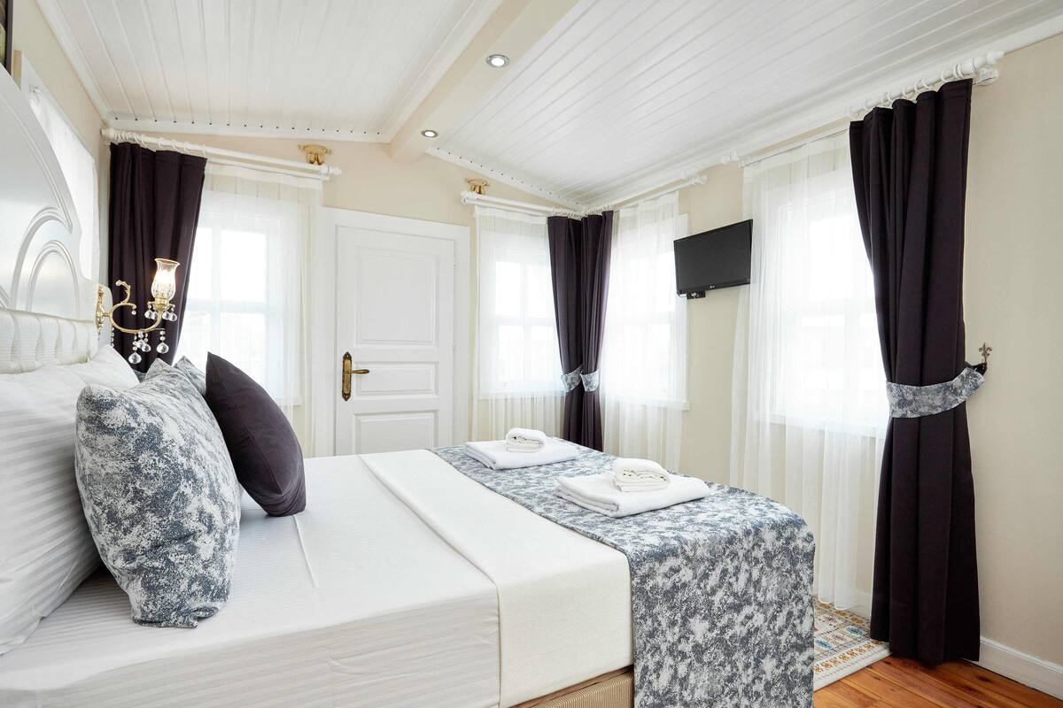Et pænt og ryddeligt hotelværelse med seng, puder, et fladskærms-tv og et vindue med gardiner.