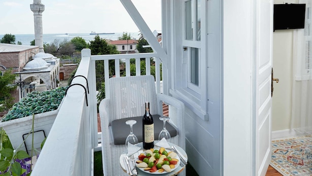 A balcony with a white railing, a wicker chair, a small table with a bottle and glasses, and a view of a mosque and sea. - Mataraci Konak (Istanbul)