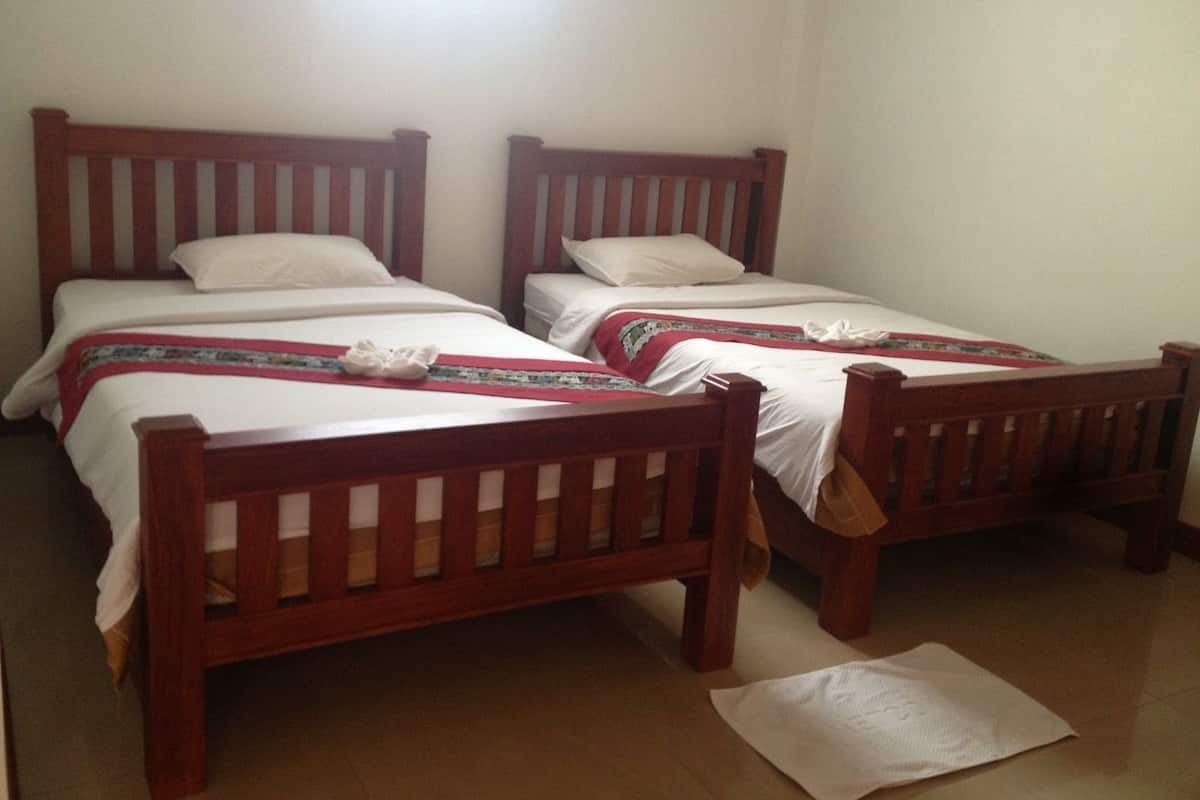 A room with two wooden beds, white bedding, and a red and green patterned blanket.