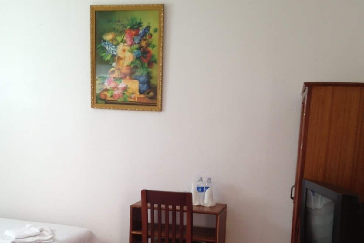 A hotel room with a bed, a wooden chair, a television, and a painting on the wall.