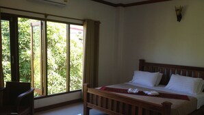 A bedroom with a wooden bed, a window with curtains, and a view of greenery outside. - Chalouvanh Hotel (Pakse)