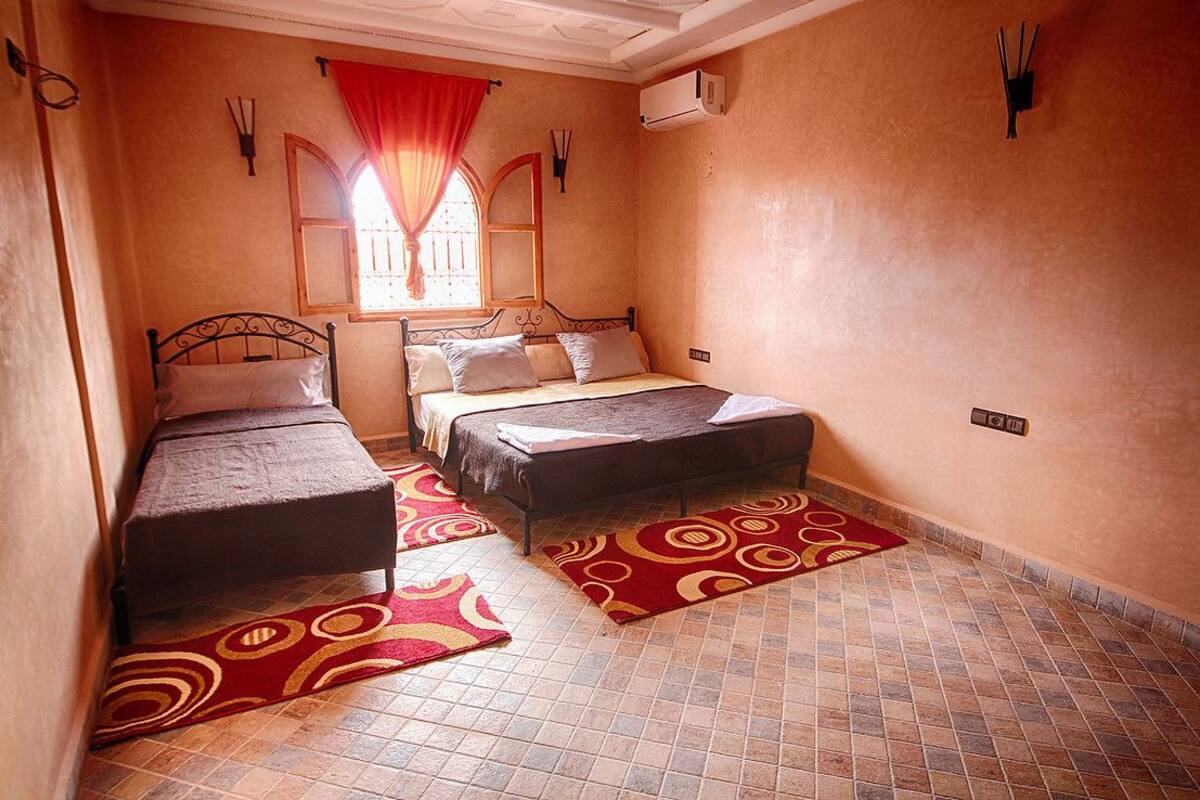 A narrow room with two beds, a window with a red curtain, and a tiled floor.