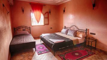Une chambre avec deux lits, une fenêtre avec des rideaux, un sol carrelé et un luminaire fixé au mur.
