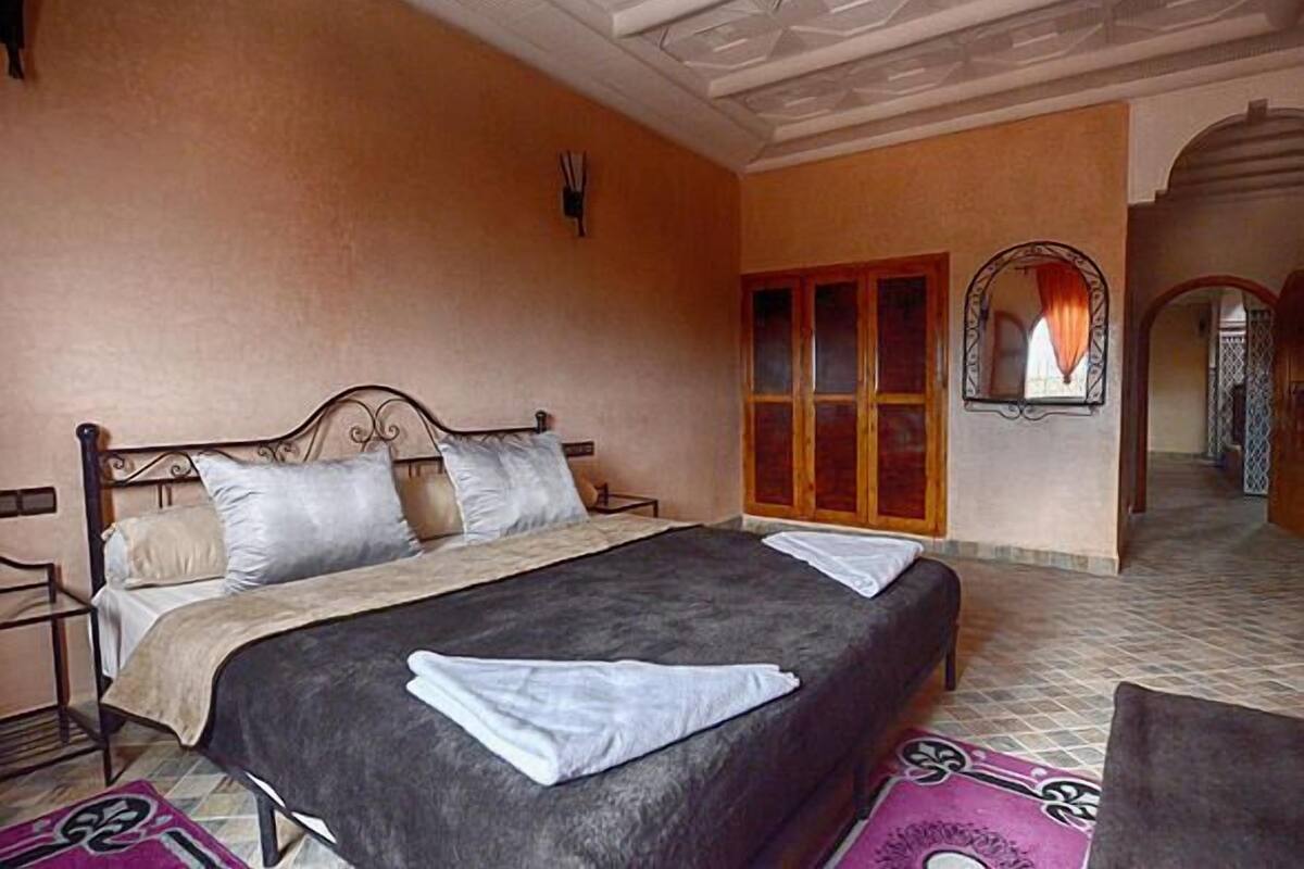 A bedroom with a bed, a wardrobe, a mirror, and a tiled floor.