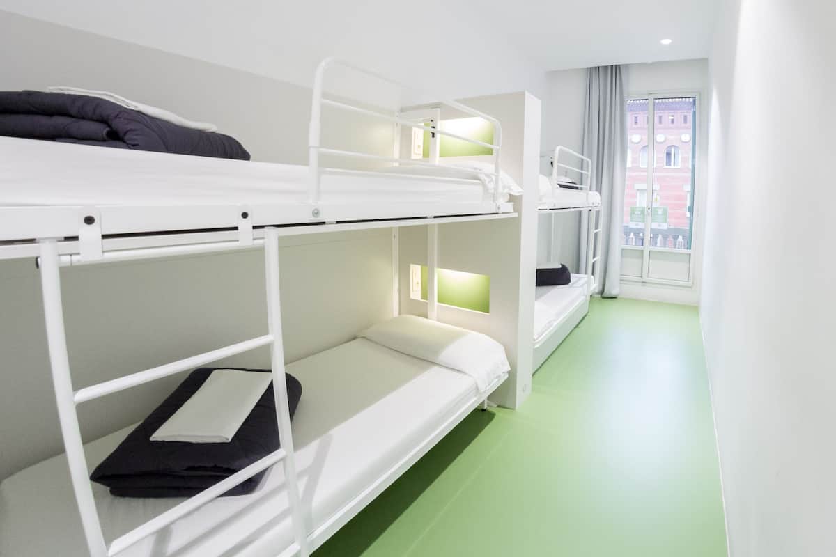 Una habitación con literas, una ventana con vista a edificios y piso verde.