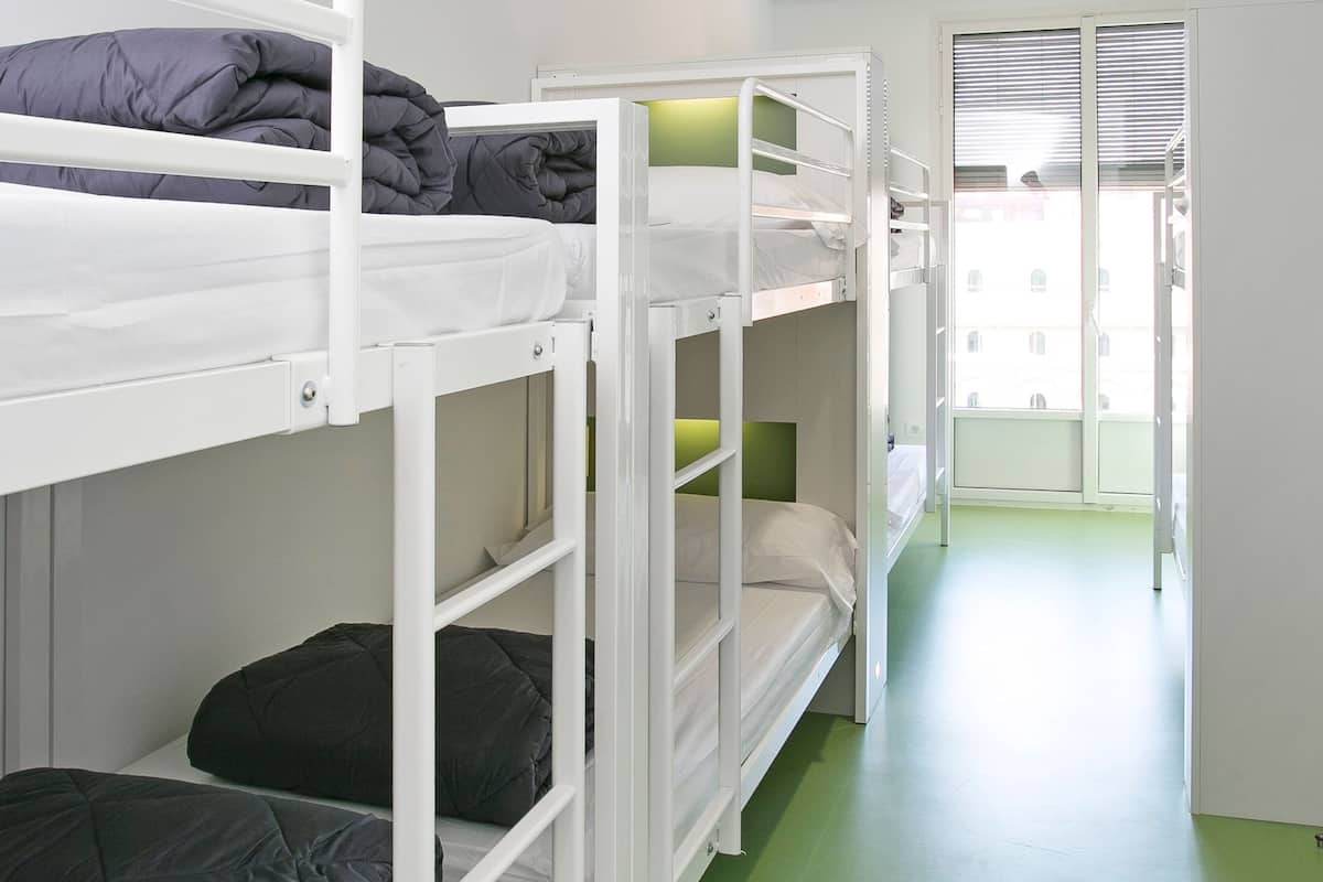 Un dormitorio con literas, una ventana con persianas y suelo verde.