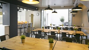 Un comedor moderno con mesas de madera y sillas negras, con iluminación colgante y plantas en macetas.