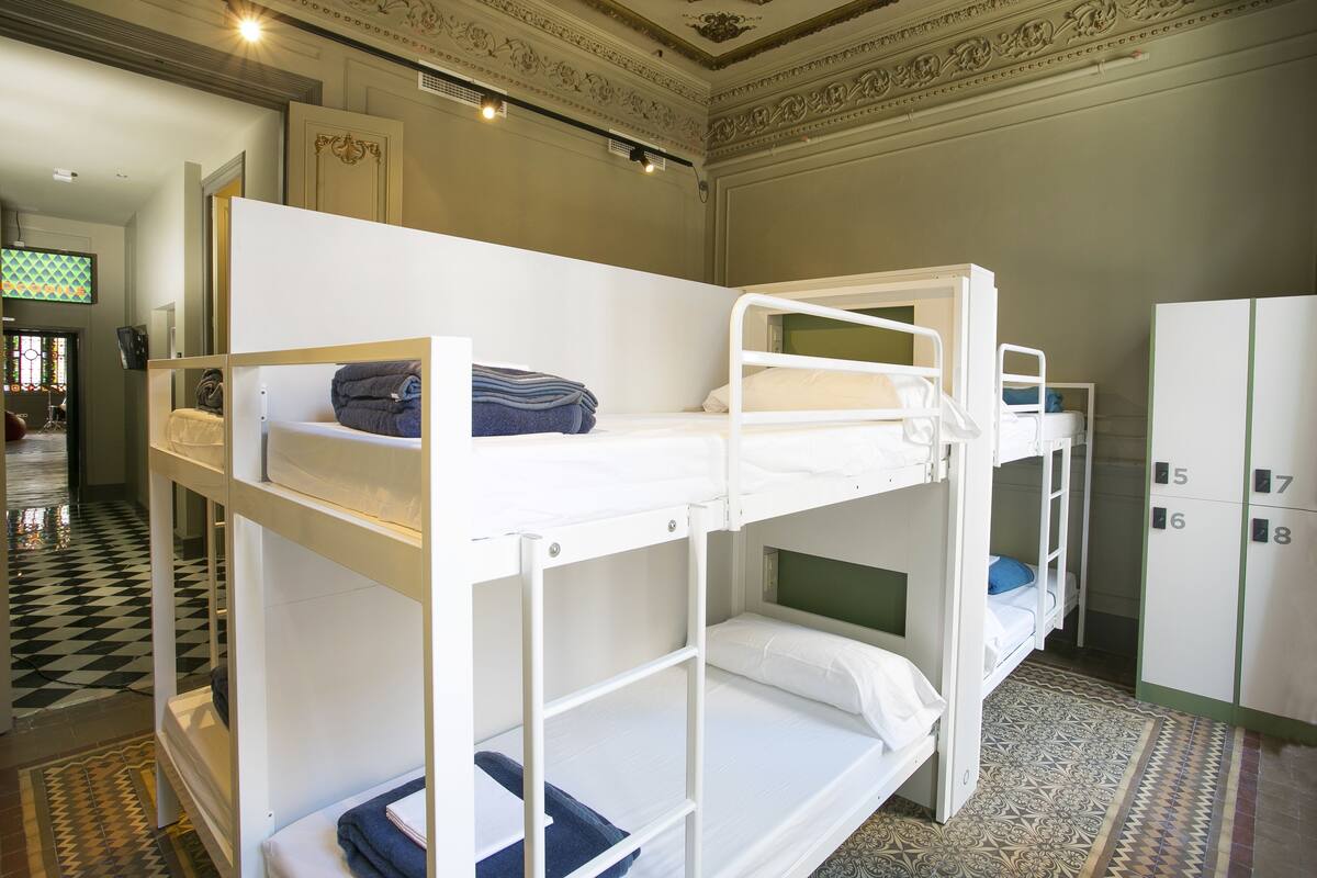 Habitación con literas, piso a cuadros, cabecera verde y armario con taquillas numeradas.