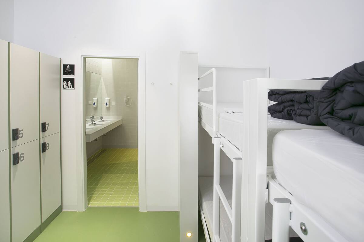 Habitación de hotel compacta con literas, baño pequeño y piso de baldosas verdes.