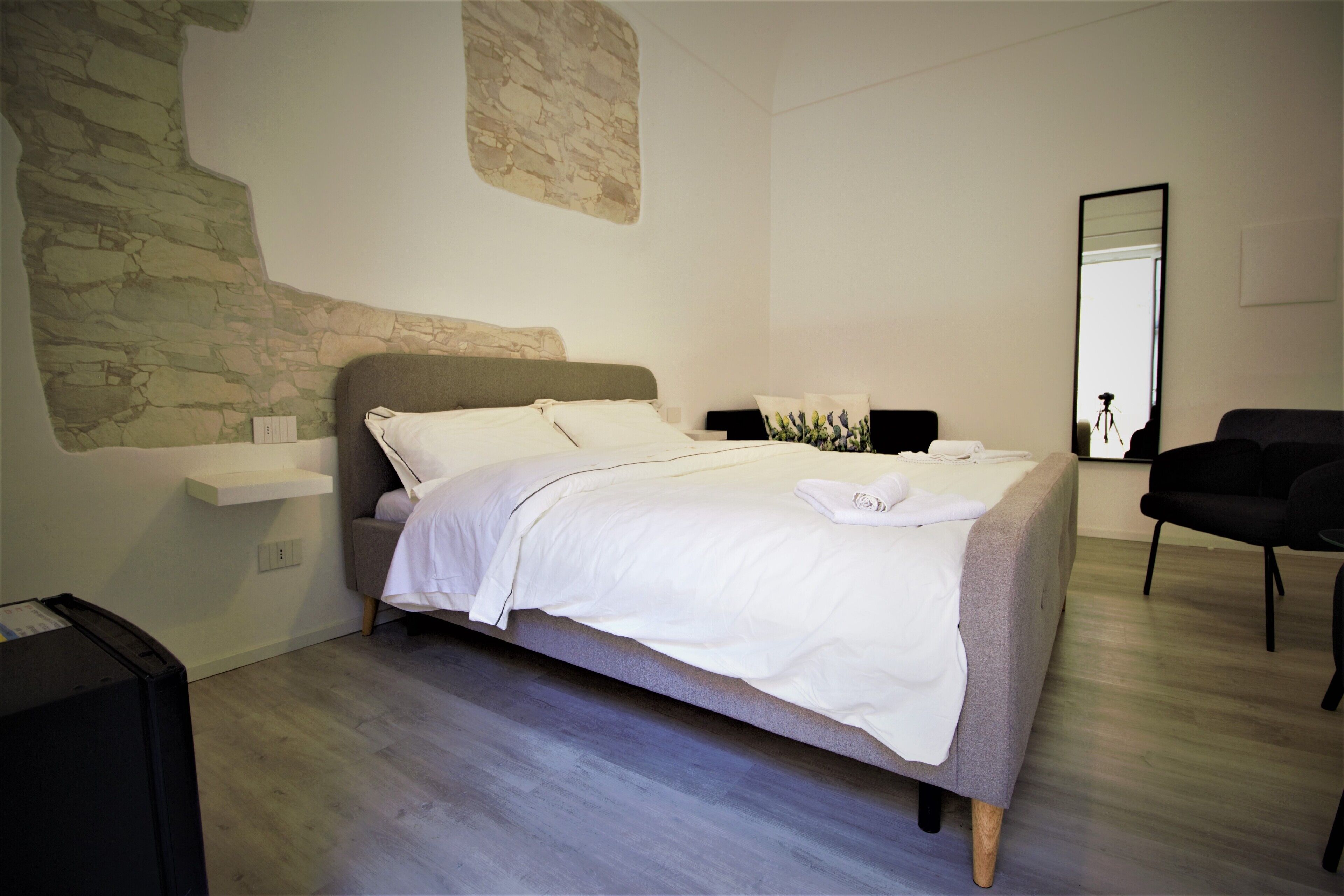 A modern bedroom with a bed, a small bedside table, a chair, and a mirror.