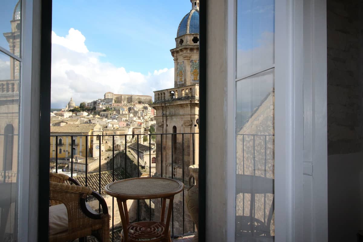 Een balkon met rieten meubilair en uitzicht op historische gebouwen en een toren.