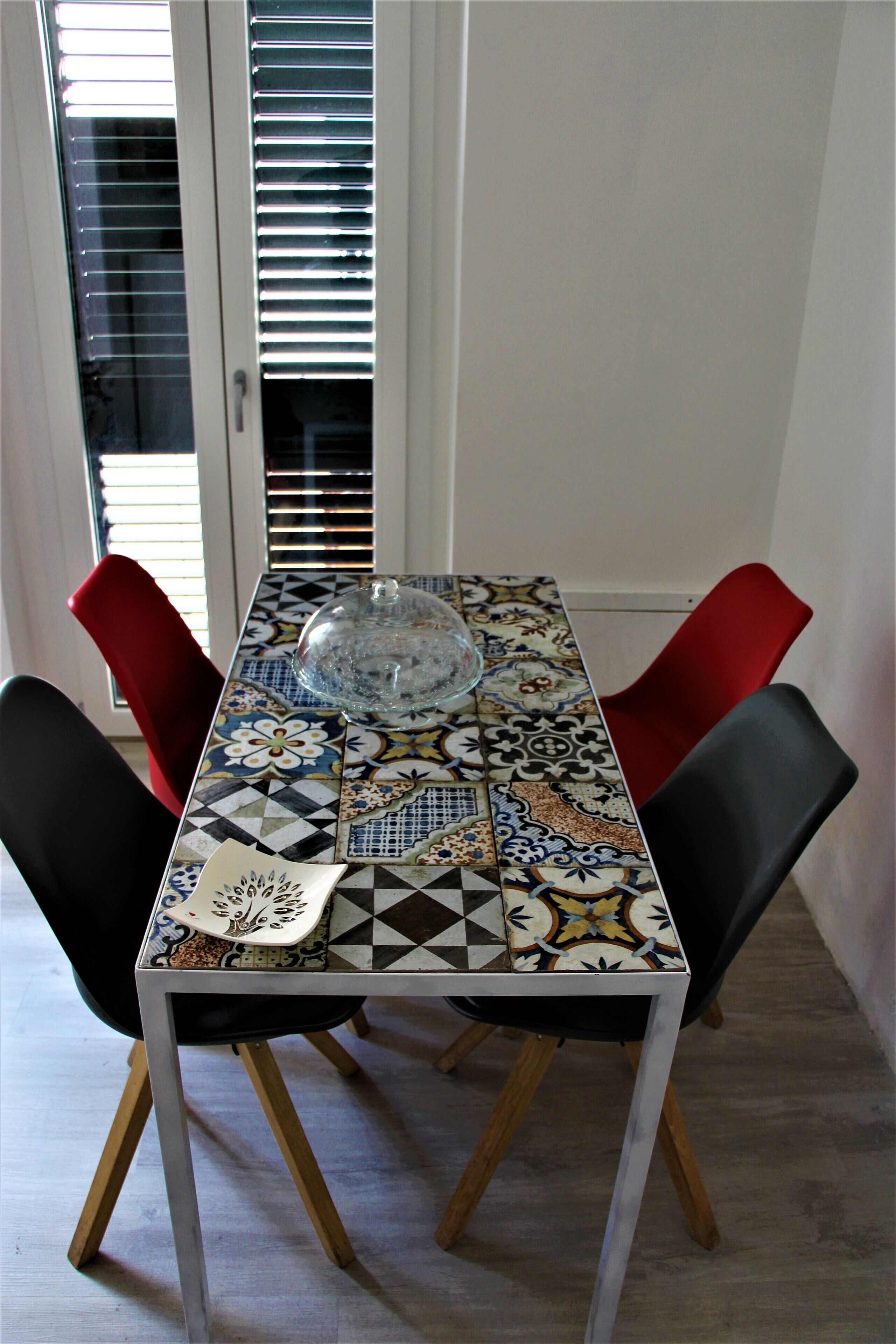 Una mesa de comedor con mantel estampado, dos sillas rojas y una lámpara de cristal en el centro.