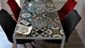 Una mesa de comedor con mantel estampado, dos sillas rojas y una lámpara de cristal en el centro.