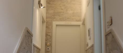 Un pasillo estrecho con paredes de piedra y suelo de madera, que conduce a una puerta blanca.