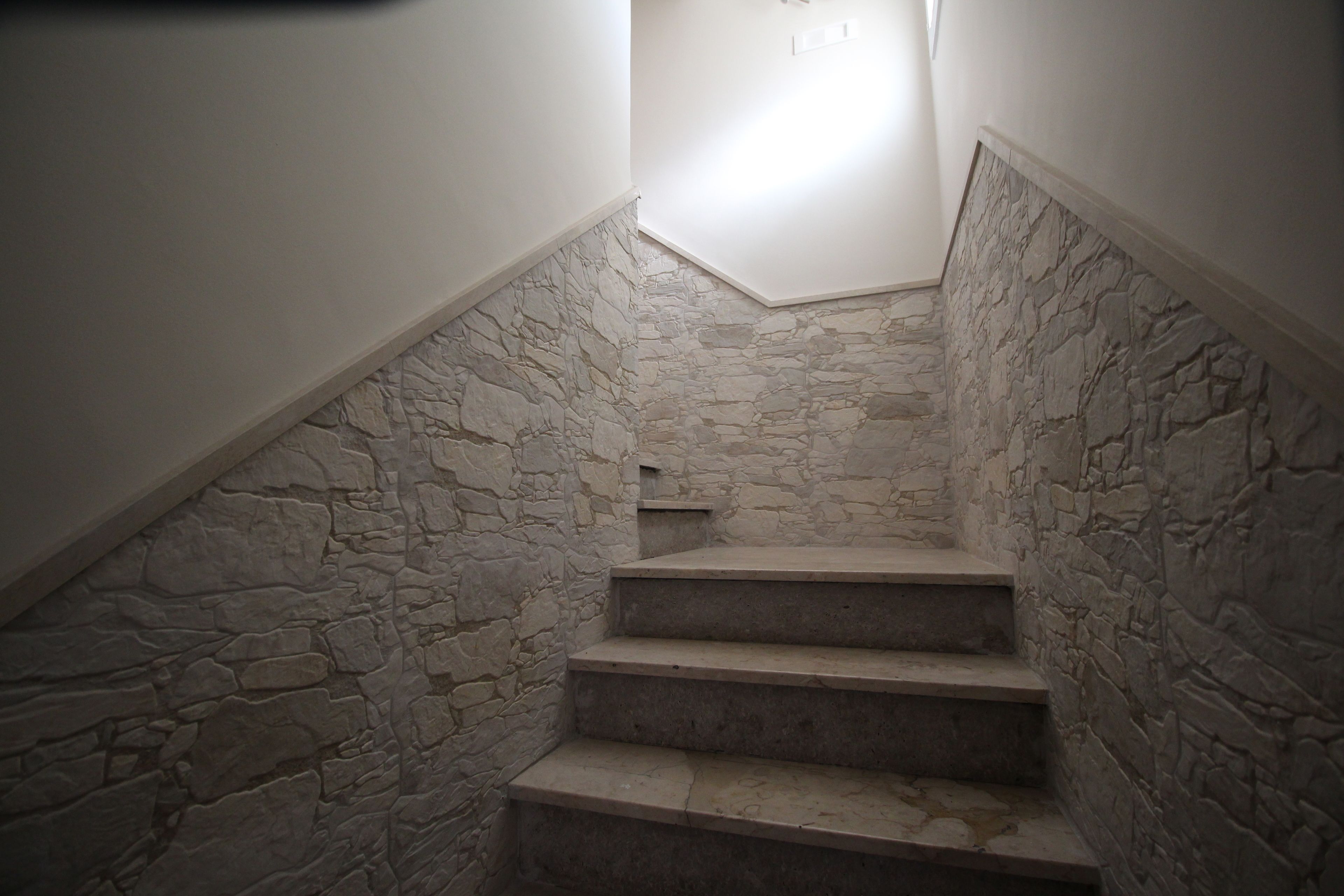 Un escalier avec des murs en pierre et un luminaire au sommet.