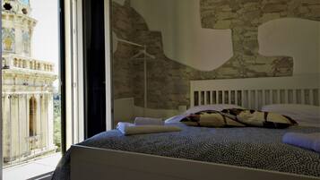 Une chambre à coucher avec un grand lit, une tête de lit blanche et une vue sur un bâtiment historique par une fenêtre ouverte.