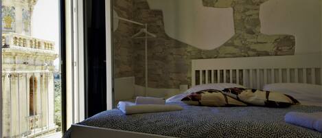 Un dormitorio con una cama grande, un cabecero blanco y vistas a un edificio histórico a través de una ventana abierta.
