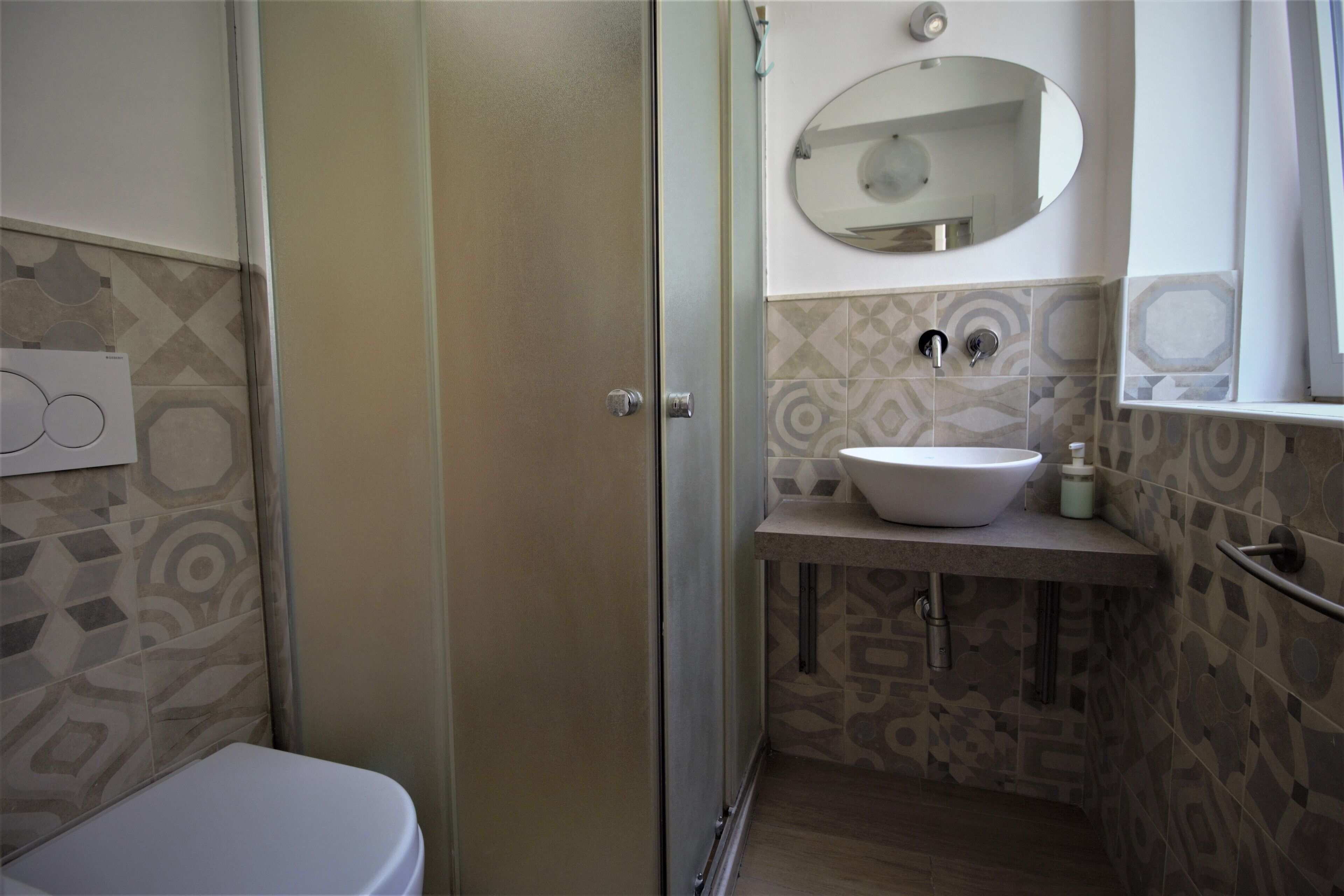 A bathroom with a toilet, a sink, a mirror, and patterned tiles.