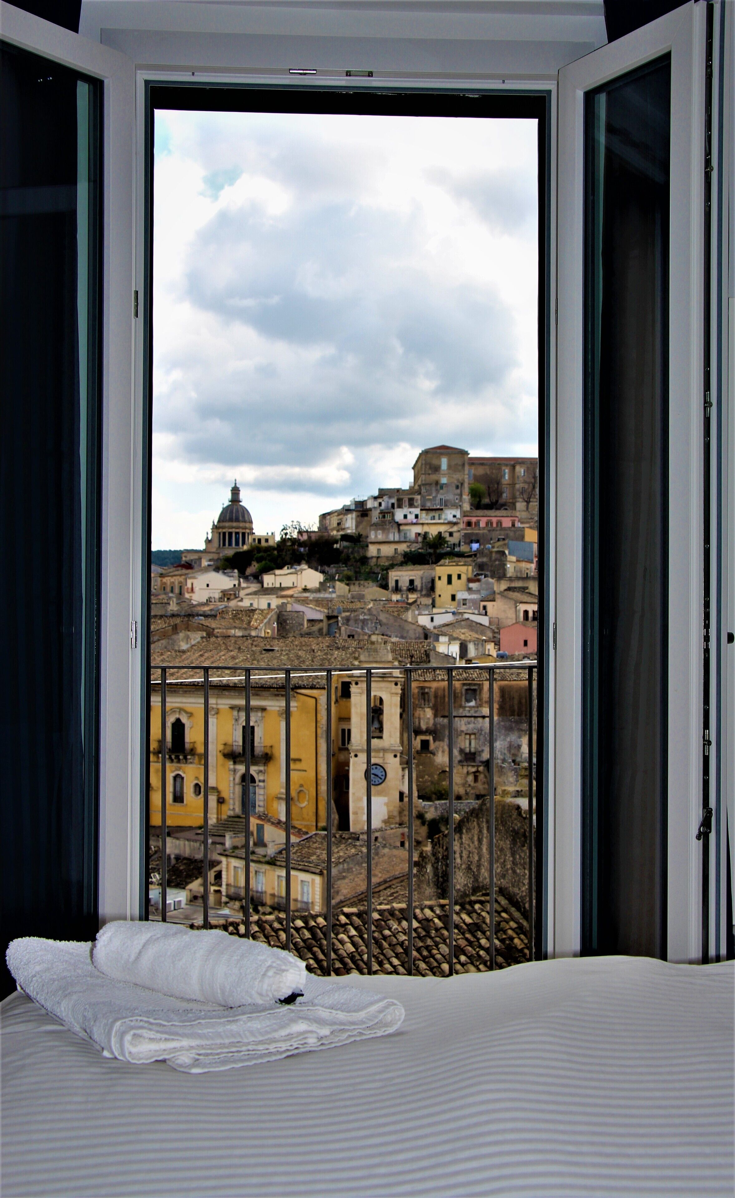A hotel room with a balcony overlooking a cityscape, featuring historic buildings and a dome structure.
