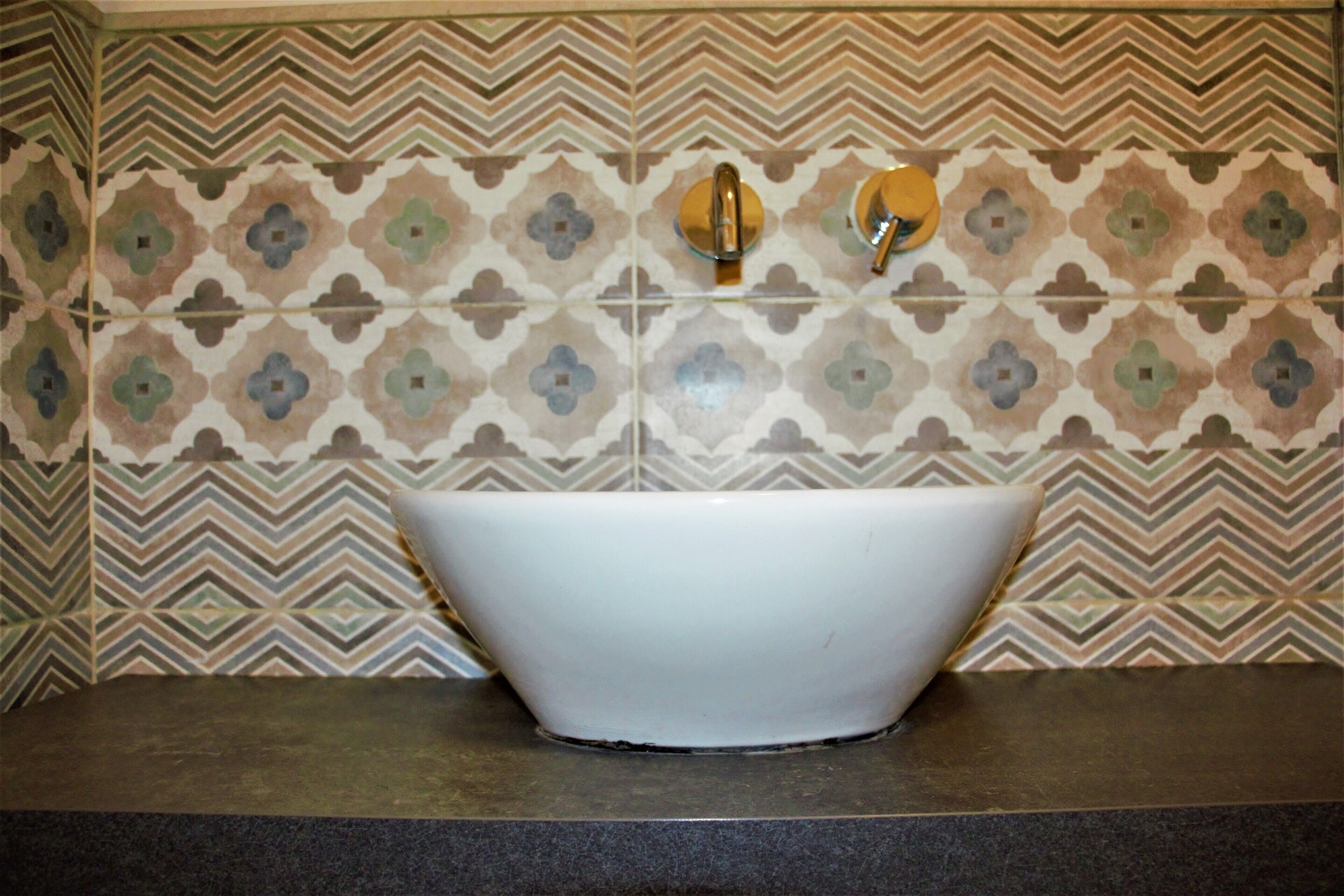 Un baño con lavamanos blanco, un espejo y un salpicadero de azulejos estampados.