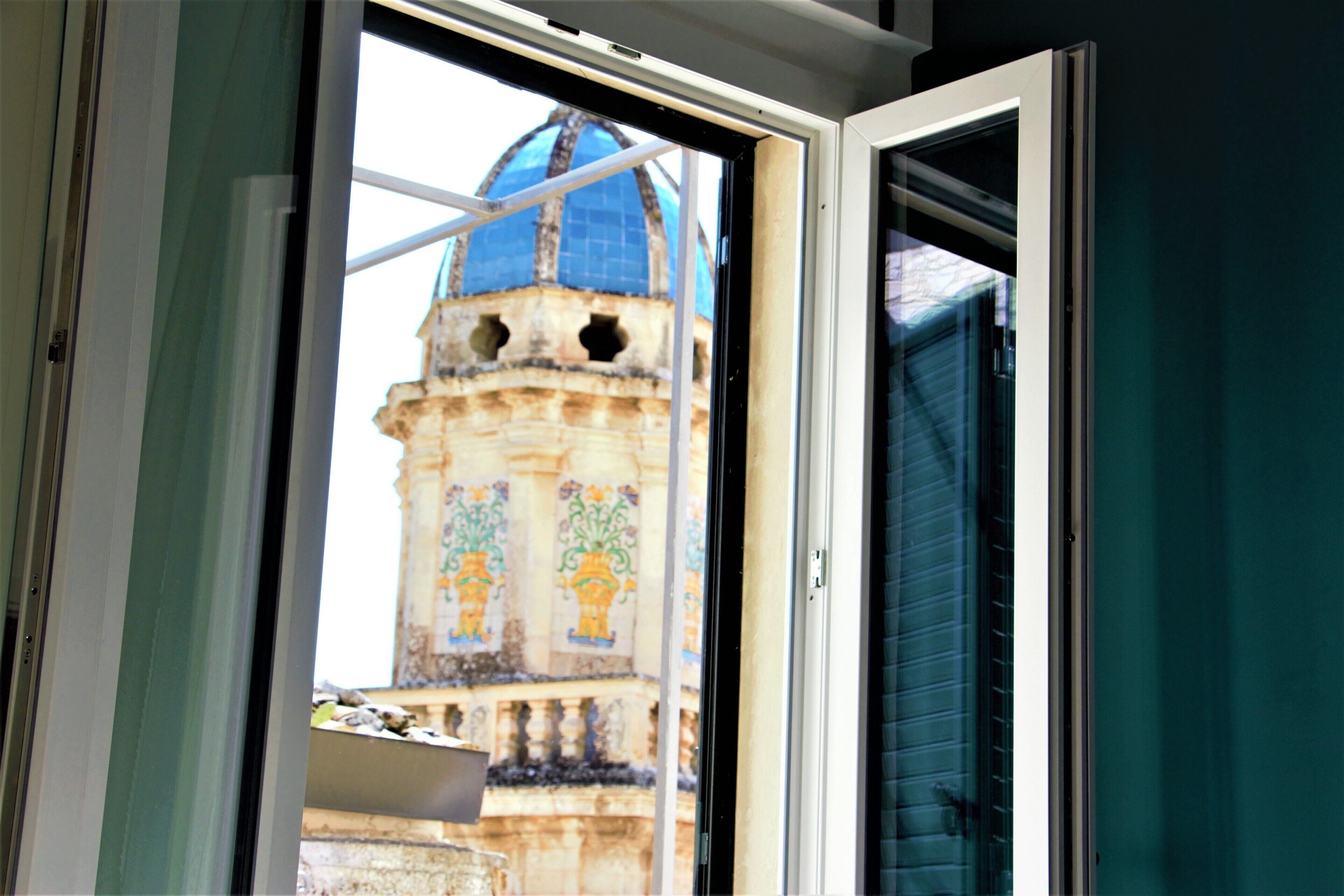 Ein offenes Fenster mit Blick auf ein historisches Gebäude mit Kuppel und aufwendiger Fassade.