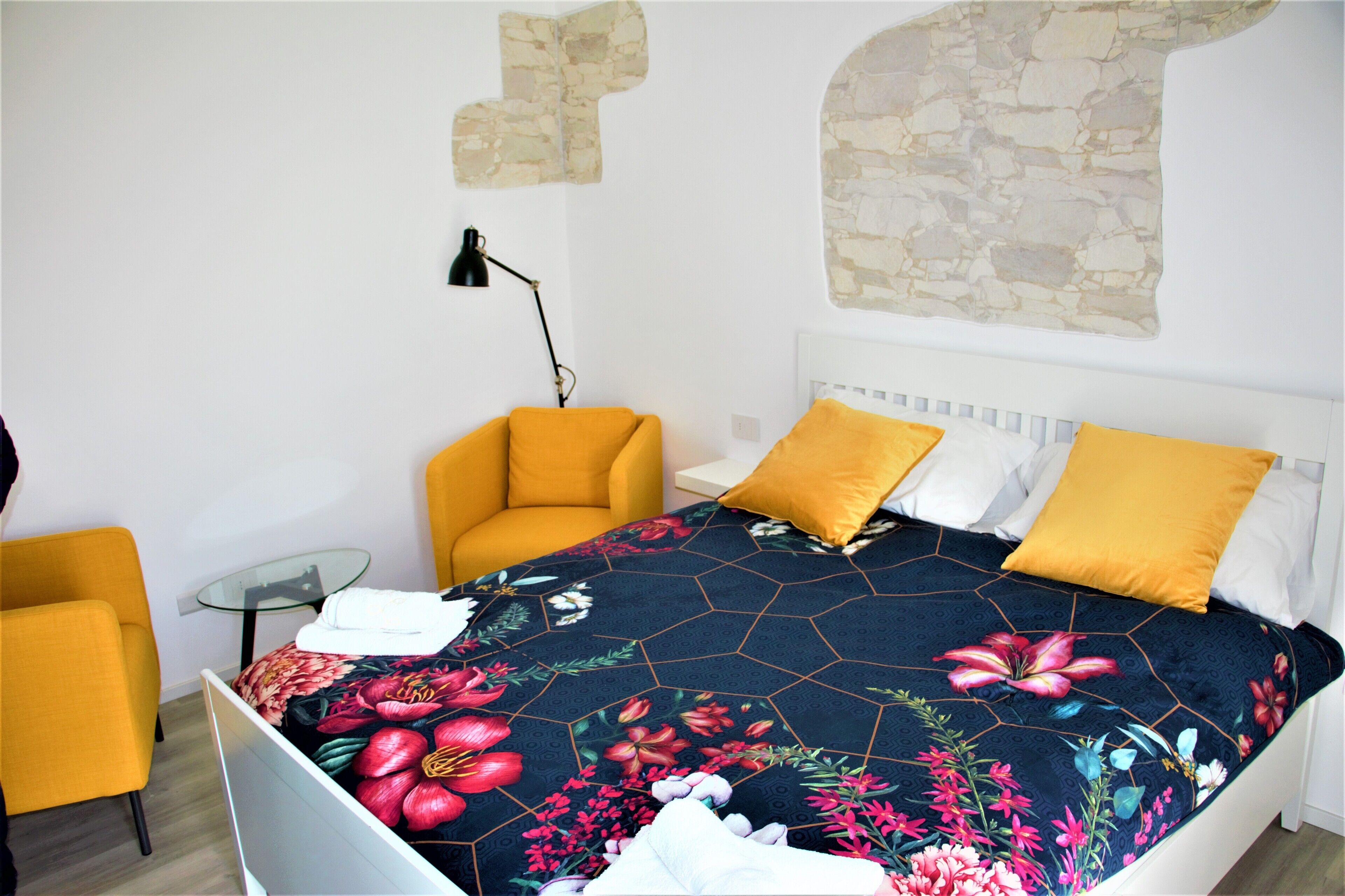 Une chambre à coucher avec un lit, deux chaises jaunes, une petite table et une lampe.