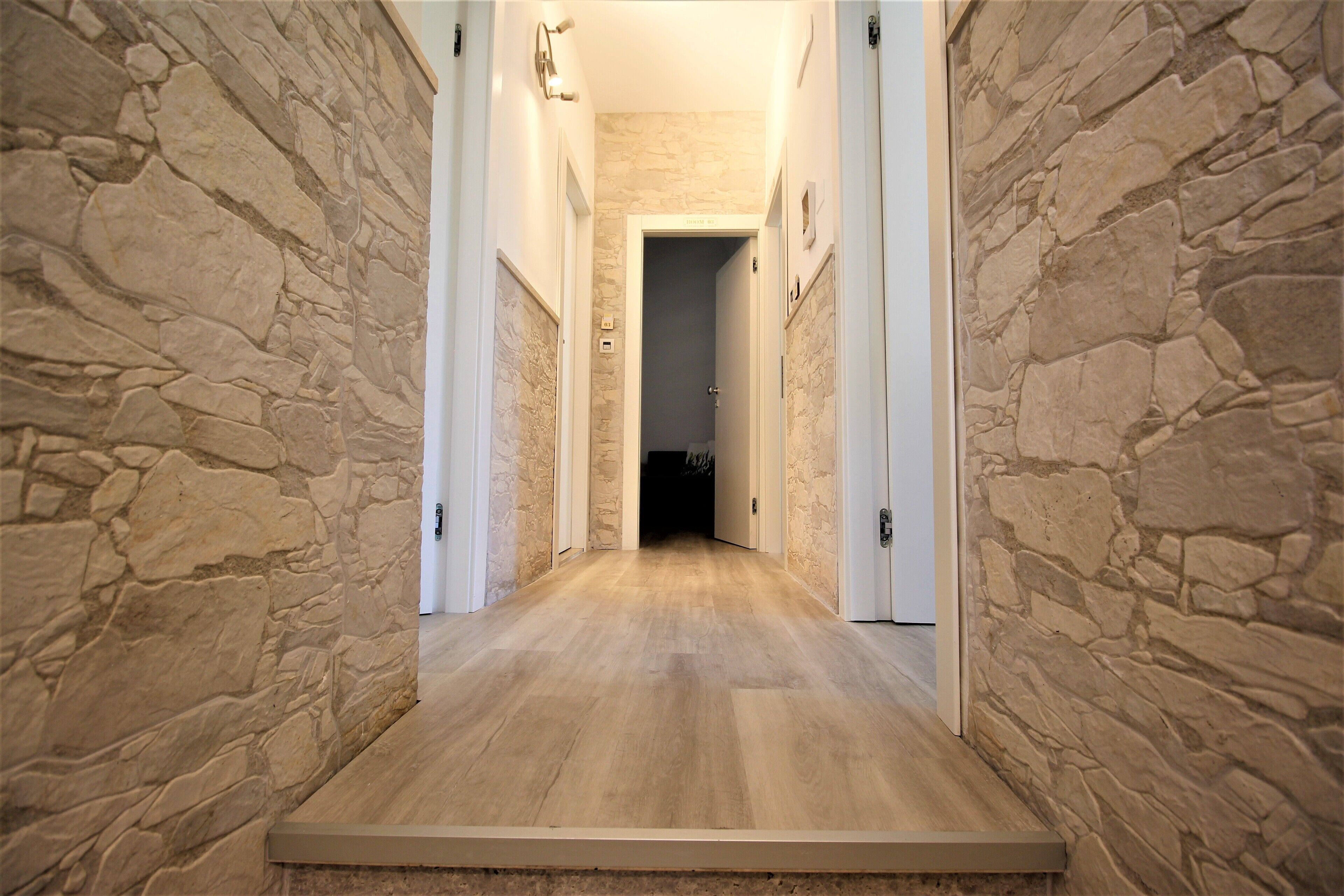 A hallway with stone walls and wooden flooring leading to a door.