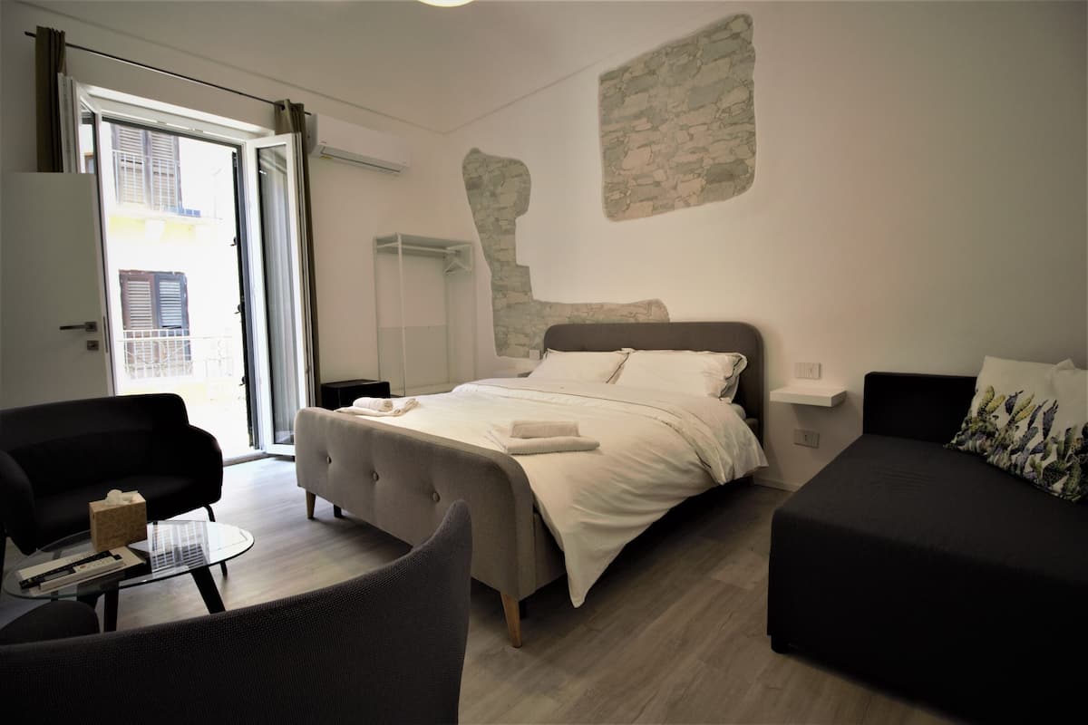 Een moderne slaapkamer met een groot bed, een bank, een tafeltje en een balkon.