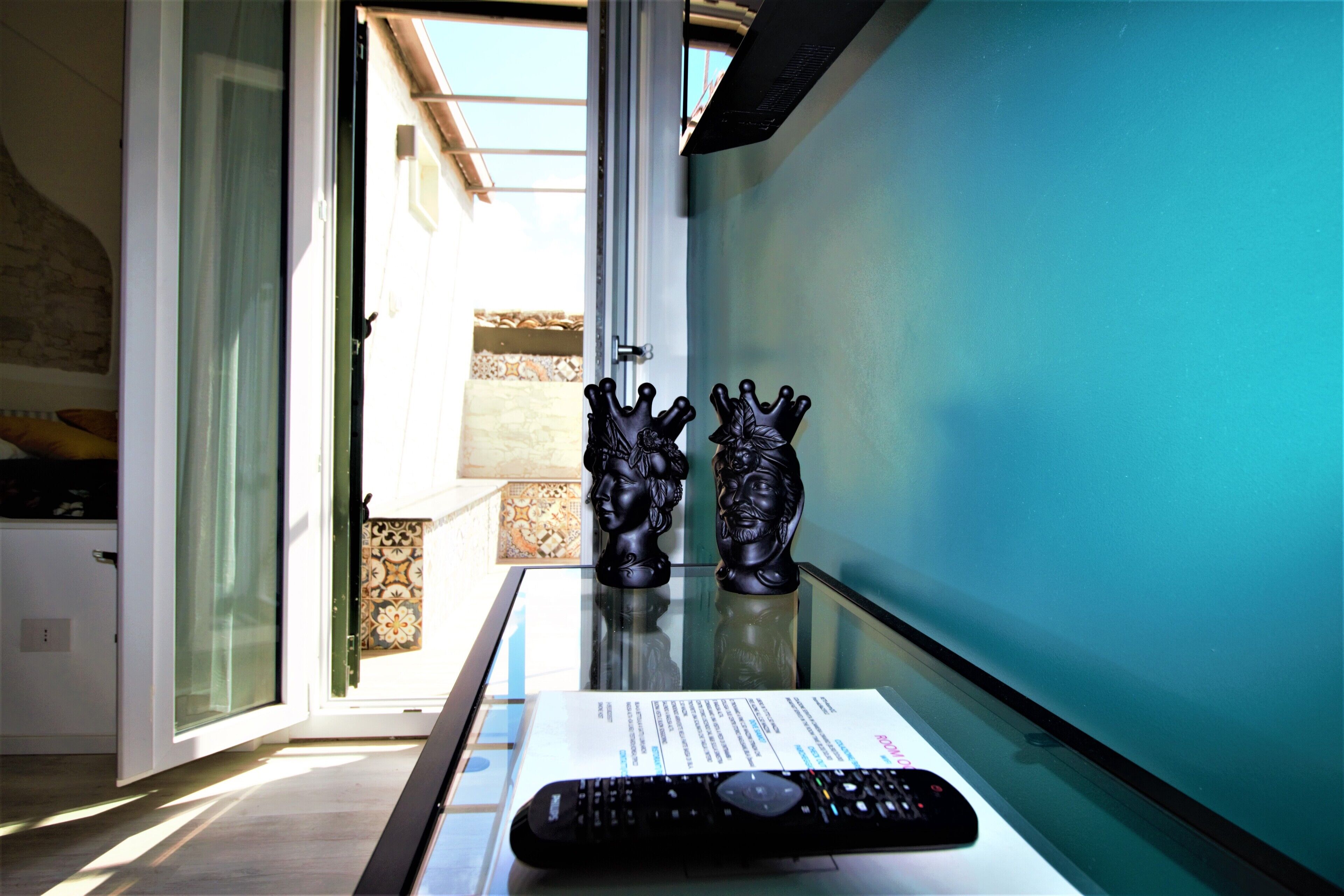 A remote control on a glass table with two decorative busts and a document.