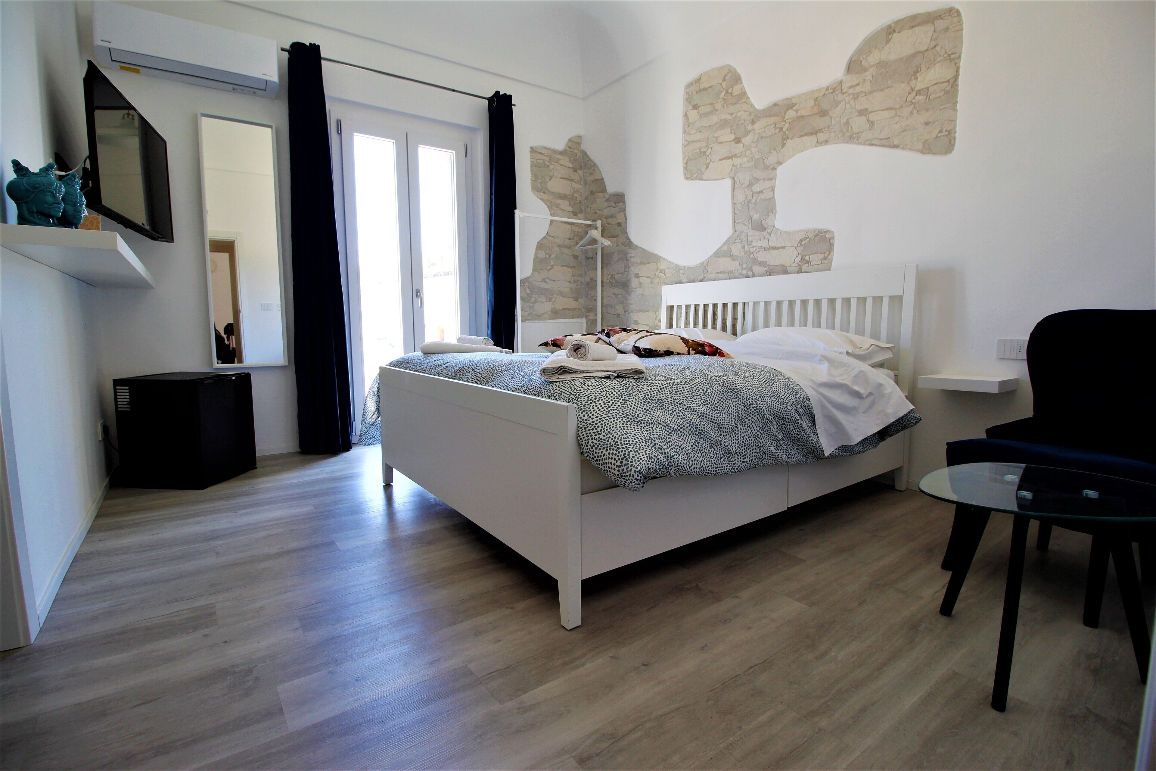 Un dormitorio moderno con cama blanca, una silla negra y una pared de piedra decorativa.
