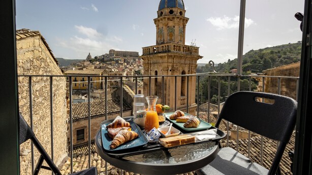 Un balcón con una mesa dispuesta para el desayuno, con vistas a un casco antiguo y una torre destacada.
