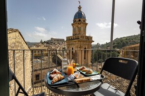 Un balcon avec une table dressée pour le petit-déjeuner, offrant une vue sur un paysage urbain historique dominé par une tour imposante.