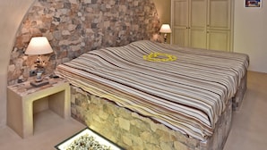 A bedroom with a stone arch wall, a bed with striped bedding, two bedside lamps, a stone floor, and a wardrobe. - Tinos Aqua Palazzo (Tinos)