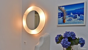 A bathroom with a white sink, a round mirror with a light, and a vase with blue flowers. - Tinos Aqua Palazzo (Tinos)