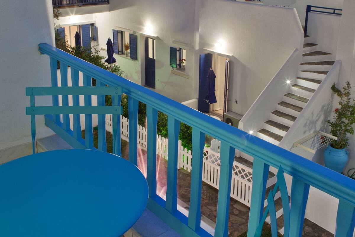 Ein mehrstöckiger Innenhof mit blauer Brüstung, einer weißen Treppe und einem blauen Tisch.