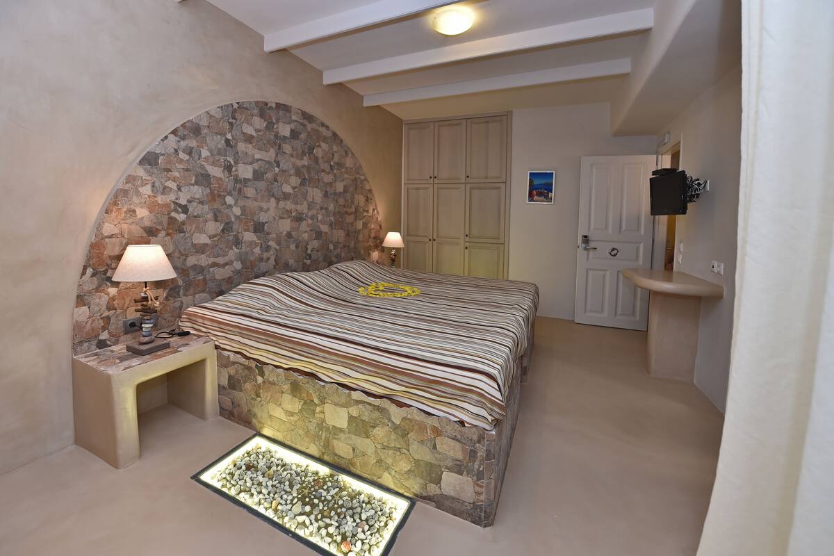 Ein Schlafzimmer mit Steinwand, einem Bett mit gestreifter Bettwäsche, einem Nachttisch mit Lampe, einem kleinen Teppich und einer Tür mit Spiegel.