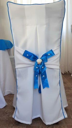 A chair with a white cover and a blue ribbon tied around the middle.