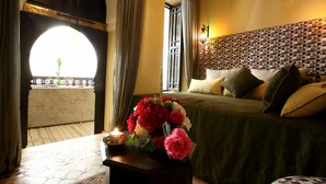 Quarto com cama, vaso de flores, mesa de cabeceira e janela com cortinas.