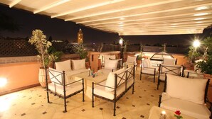 Um terraço no telhado com área de estar ao ar livre, plantas em vasos e vista para uma torre ao fundo.