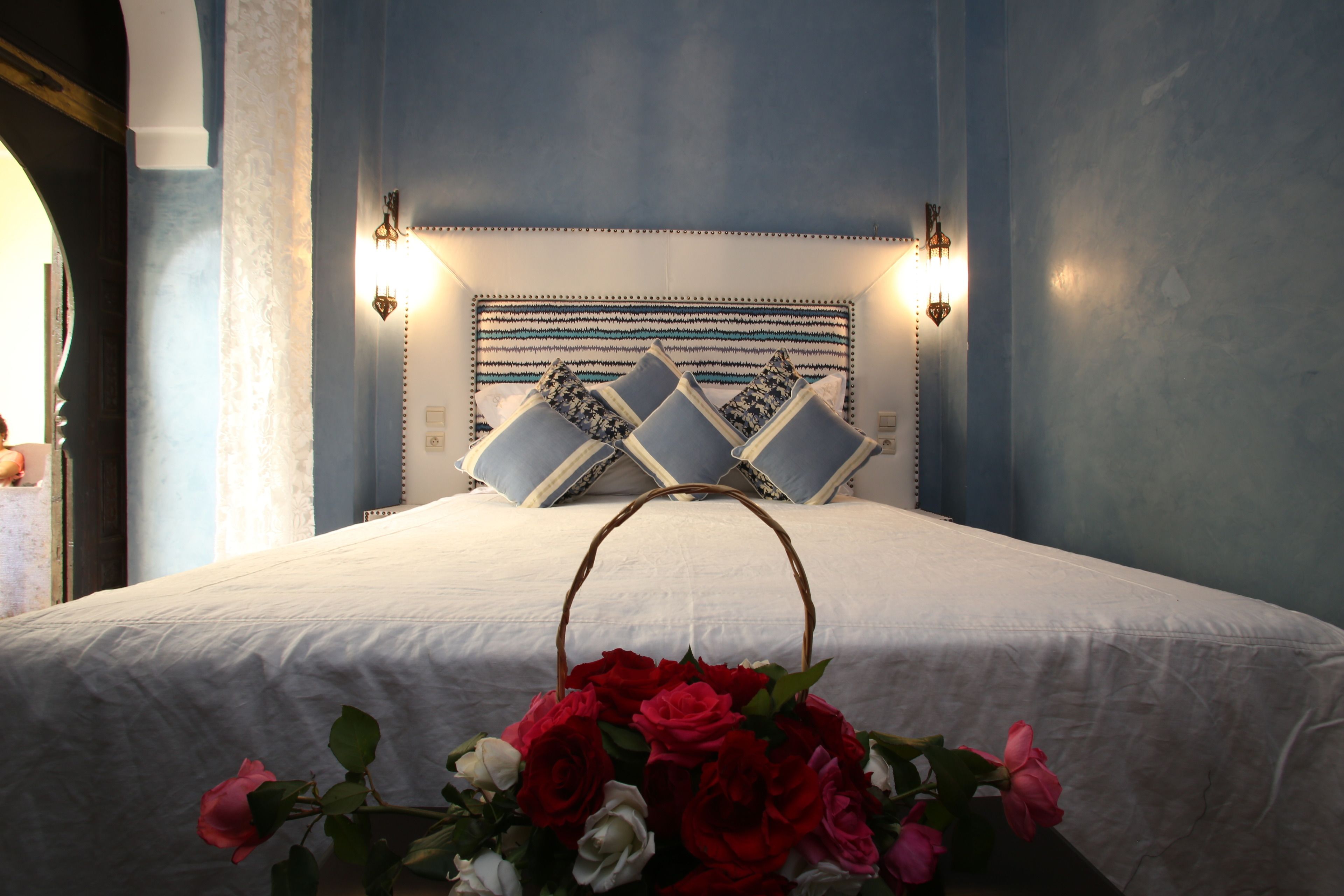 Una cama bien hecha con una colcha blanca y un arreglo floral al pie.