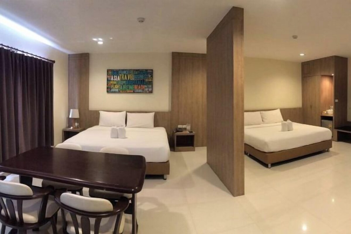 A hotel room with a large bed, a smaller bed, a dining table with chairs, and a wall with a colorful poster.