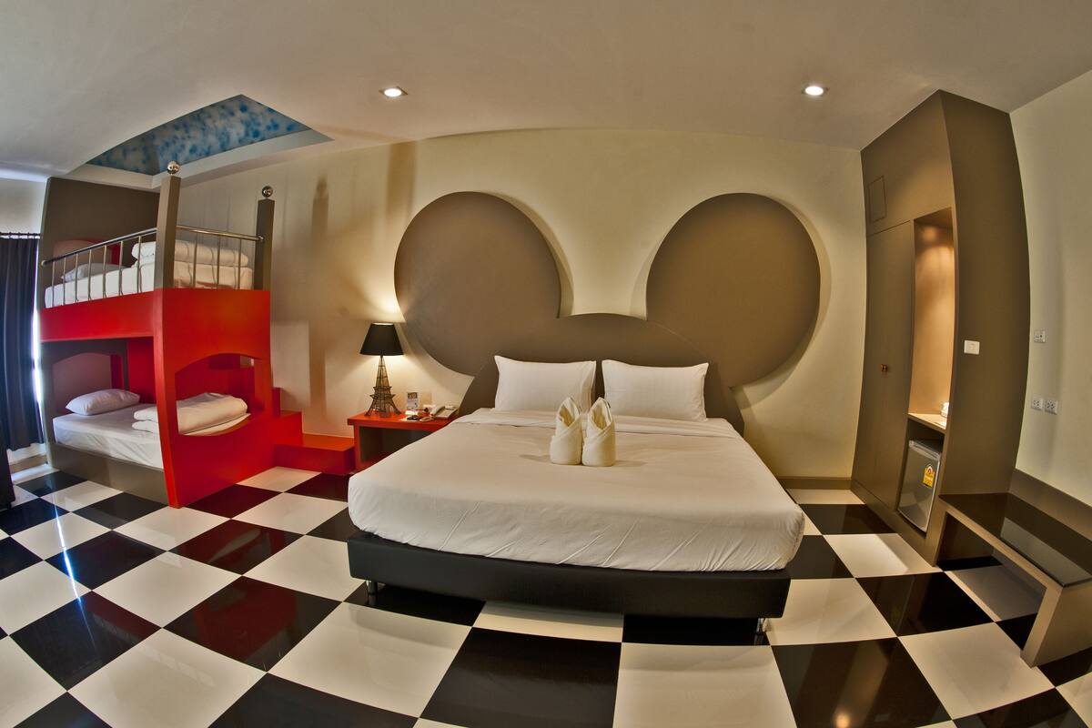 Una habitación de hotel con piso a cuadros, una cama grande con ropa blanca, una cama individual roja y un diseño de pared único.