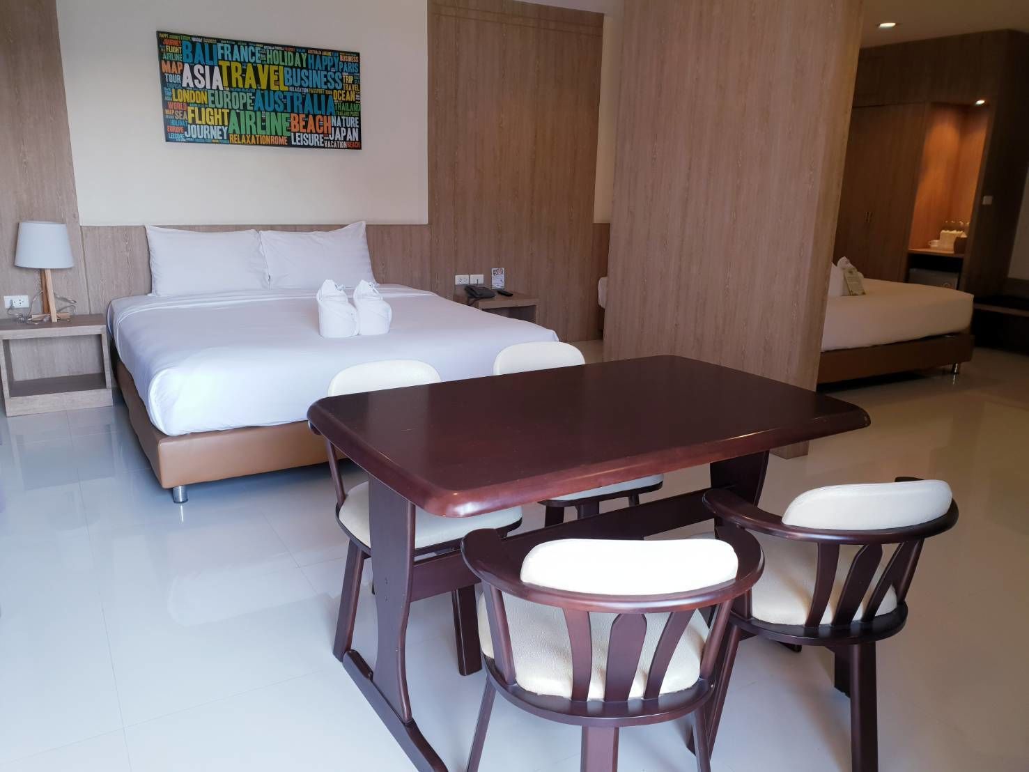 Una habitación de hotel moderna con una cama grande, una mesa de comedor con sillas y una obra de arte con una nube de palabras en la pared.