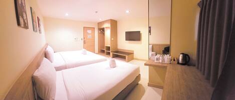 A hotel room with two beds, a wooden desk with a kettle, and a flat-screen TV on the wall.