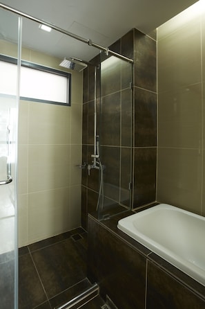 A modern bathroom with a glass shower enclosure, a bathtub, and dark tiled walls.